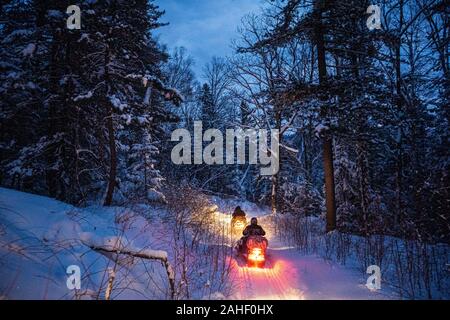 Motoneige dans la soirée passe par la forêt d'hiver. phares. nuit route à travers la forêt d'hiver. motoneige à la nuit. Banque D'Images