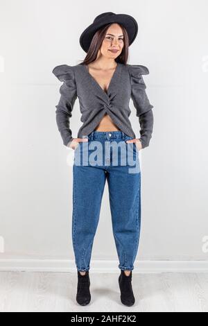 Cute young woman in sweater et jeans à marcher en direction de caméra avec les mains dans les poches. Corps plein isolé sur fond blanc. Banque D'Images