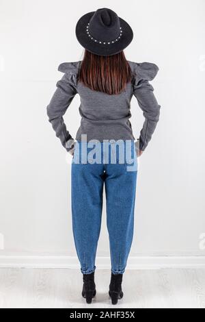 Cute young woman in sweater et jeans à marcher en direction de caméra avec les mains dans les poches. Corps plein isolé sur fond blanc. Banque D'Images