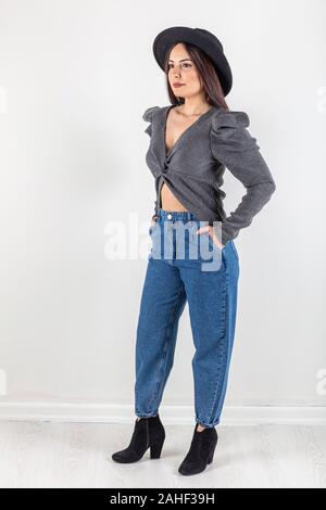 Cute young woman in sweater et jeans à marcher en direction de caméra avec les mains dans les poches. Corps plein isolé sur fond blanc. Banque D'Images