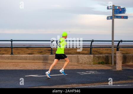 Southport, Merseyside, Royaume-Uni. 29 décembre 2019 Météo France. Des couleurs vives, des vêtements haute visibilité jaune, sur un fond gris pour la journée aussi sportive les résidents de prendre exercice tôt sur le front de la promenade côtière au nord-ouest de la station balnéaire. Credit : MediaWorldImages/Alamy Live News Banque D'Images