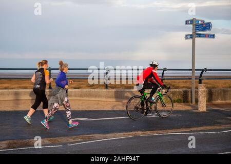 Southport, Merseyside, Royaume-Uni. 29 décembre 2019 Météo France. Des couleurs vives, des vêtements haute visibilité rouge, sur un fond gris pour la journée aussi sportive les résidents de prendre exercice tôt sur le front de la promenade côtière au nord-ouest de la station balnéaire. Credit : MediaWorldImages/Alamy Live News Banque D'Images