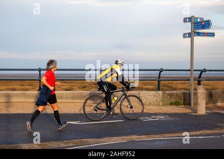 Southport, Merseyside, Royaume-Uni. 29 décembre 2019 Météo France. Des couleurs vives, rouge et jaune Vêtements haute visibilité, sur un fond gris pour la journée aussi sportive les résidents de prendre exercice tôt sur le front de la promenade côtière au nord-ouest de la station balnéaire. Credit : MediaWorldImages/Alamy Live News Banque D'Images