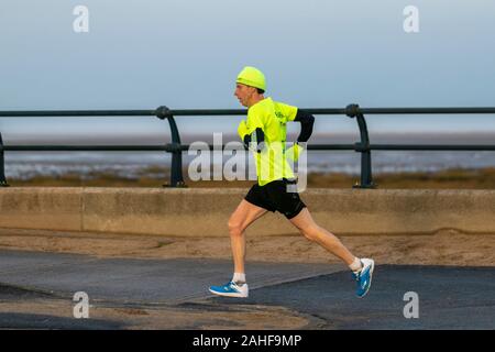 Southport, Merseyside, Royaume-Uni. 29 décembre 2019 Météo France. Des couleurs vives, des vêtements haute visibilité, sur un fond gris pour la journée, comme les résidents de prendre de l'exercice tôt le matin sur la promenade du front de mer du nord-ouest de la station balnéaire. Credit : MediaWorldImages/Alamy Live News Banque D'Images