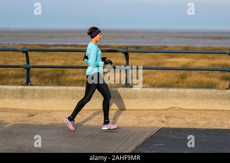 Southport, Merseyside, Royaume-Uni. 29 décembre 2019 Météo France. Des couleurs vives, des vêtements haute visibilité bleu, sur un fond gris pour la journée aussi sportive les résidents de prendre exercice tôt sur le front de la promenade côtière au nord-ouest de la station balnéaire. Credit : MediaWorldImages/Alamy Live News Banque D'Images