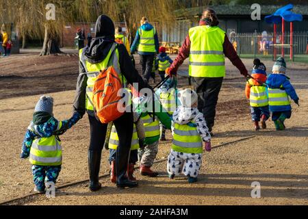 Un groupe de jeunes enfants de l'école ou la crèche de enfants vêtus de gilets haute visibilité tout en marchant avec les enseignants Banque D'Images