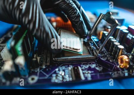 Réparateur ingénieur tenant les mains dans des gants noirs, CPU Processeur à puce à insérer dans le connecteur de la carte mère de l'ordinateur. La notion de technologie Banque D'Images