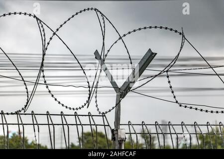 Les spirales de fil barbelé sur une clôture, sur un fond de nuages sombres. Protection de la zone avec une courbe de barbelés. Banque D'Images