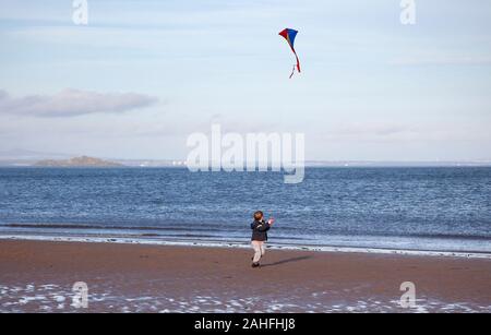 La plage de Portobello, Édimbourg, Écosse, Royaume-Uni. 29 décembre 2019. La température à 11 degrés plus doux, avec une faible brise soleil sur la côte d'encourager les gens à sortir sur la plage de sable, un jeune garçon et son père le fait bien pour obtenir leurs cerfs-volants colorés et un mode femme portant des bottes rouge vif avec ses dalmatiens et entouré par deux autres chiens. Credit : Arch Blanc/ Alamy Live News. Banque D'Images