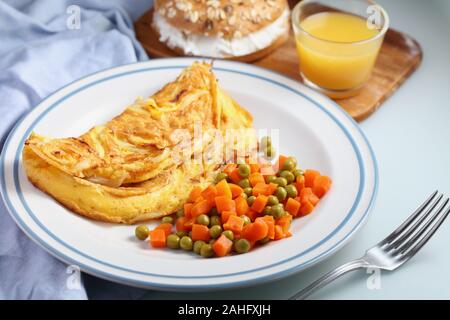 Petit déjeuner avec omelette française, salade de petits pois et carottes, sandwich au bagel au fromage doux et une tasse de jus d'orange en gros plan Banque D'Images