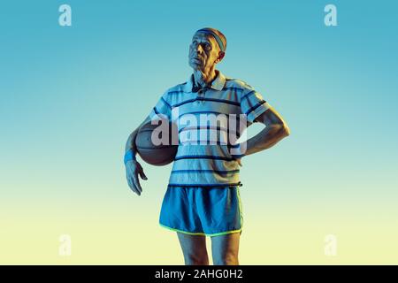 Senior man wearing sportwear jouer au basket-ball sur fond dégradé, neon light. Modèle homme de race blanche dans la grande forme reste actif. Concept de sport, activité, mouvement, bien-être, la confiance. Banque D'Images