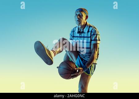 Senior man wearing sportwear jouer au basket-ball sur fond dégradé, neon light. Modèle homme de race blanche dans la grande forme reste actif. Concept de sport, activité, mouvement, bien-être, la confiance. Banque D'Images