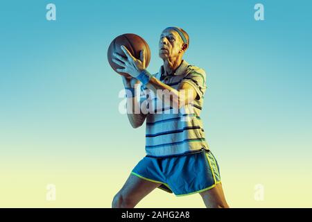 Senior man wearing sportwear jouer au basket-ball sur fond dégradé, neon light. Modèle homme de race blanche dans la grande forme reste actif. Concept de sport, activité, mouvement, bien-être, la confiance. Banque D'Images