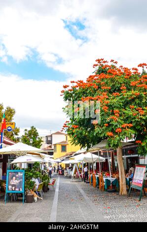 Funchal, Madeira, Portugal - Sep 10, 2019 : dans la rue pittoresque capitale de Madère avec des restaurants et cafés typiques. Les gens de boire et manger sur les terrasses en plein air dans l'arrière-plan. Photo verticale. Banque D'Images