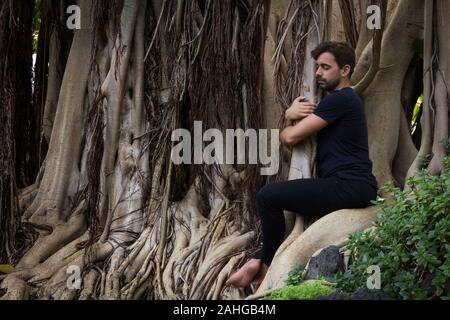 Jeune homme hugs banyan tree au jardin botanique. Beau hipster en contact avec l'environnement naturel. La conservation, la protection, la nature des concepts d'amour Banque D'Images