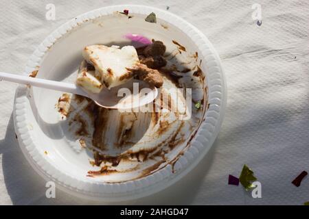 Les restes de gâteau au chocolat sur la plaque en plastique et une cuillère. Coupe dessert sucré sur du papier blanc tapis de table et de confettis. Après la partie, les concepts de célébration Banque D'Images