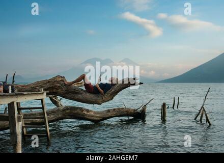 Beau, homme couché sur un arbre, la lecture dans la nature. De vie de plein air, les voyages en solo, des loisirs, du temps libre, concept éducatif. Lac Atitlan Banque D'Images