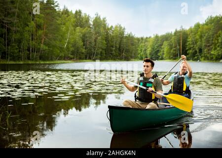 Deux hommes dans la vie gilets canoë dans le lac forestier. Surface de l'eau recouverte de nénuphars. Touristes voyageant en Finlande, ayant l'aventure. Banque D'Images