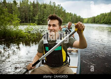 Deux hommes dans la vie gilets canoë dans le lac forestier. Surface de l'eau recouverte de nénuphars. Touristes voyageant en Finlande, ayant l'aventure. Banque D'Images