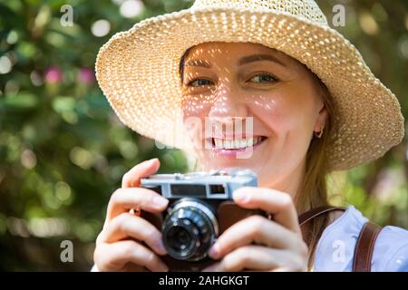 Gros plan portrait d'une belle femme en paille de chapeau de voyage dans la forêt tropicale, prenant des photos sur un appareil photo rétro. Ombres lumineuses grâce aux détails de découpe Banque D'Images