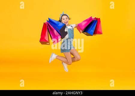 Hurry up. Acheter plus rapidement. Happy girl jump with shopping bags. Petit enfant sourire avec des sacs en papier. Préparation et célébration des fêtes. Shopping sur le black friday. Shopping d'inspiration. Traiter avec succès. Banque D'Images