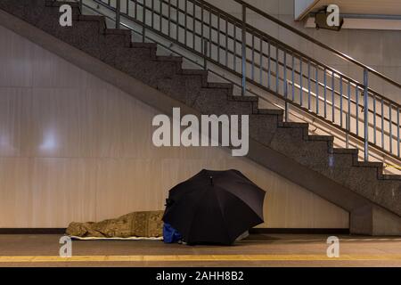 Un homme sans abri utilisant un parapluie pour ajouter à son abri dans une arcade souterraine à la station Hamamatsu, Hamamatsu, Shizuoka, Japon Banque D'Images