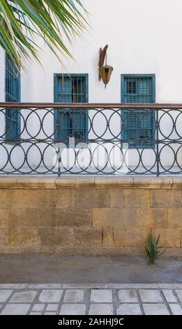 Décoratifs en fer forgé, balustrade avec main courante en bois en face de mur blanc avec trois volets vert, et lanterne vintage Banque D'Images
