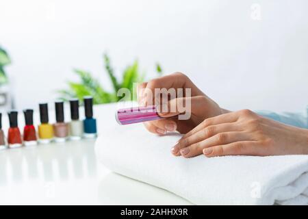 Femme à l'aide d'une lime à ongles et des ongles de forme. Vernis à ongles colorés bouteilles sur table. Femelle de broyage des ongles avec lime à ongles. Femme elle-même Banque D'Images