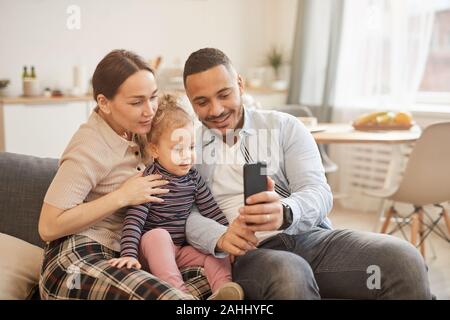 Portrait aux teintes chaleureuses de happy mixed-race family prenant en selfies hoto home intérieur, copy space Banque D'Images