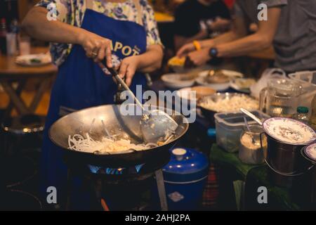 La cuisine femme mettre l'oignon couper en casserole avec les gens mangent en arrière-plan Banque D'Images