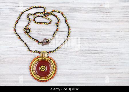 Needlecraft background - fabrication artisanale Collier avec pendentif rond en cuir marron avec des perles de verre et clairons sur planche en bois gris avec copyspa Banque D'Images