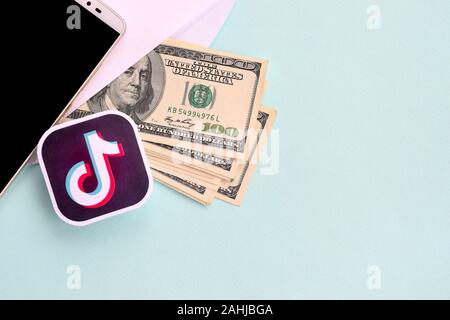 NY, USA - Le 26 décembre 2019 : logo papier Tiktok réside avec enveloppe pleine de billets d'un dollar et smartphone Banque D'Images