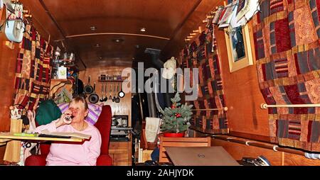 Une dame se détendre avec un verre de vin après nouveaux rideaux ont été accrochées sur son bateau étroit. Toute la scène est très chaleureux et confortable. Banque D'Images