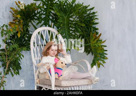 Portrait d'une belle petite fille à la mode avec un chapeau assis sur une chaise Banque D'Images