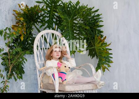 Portrait d'une belle petite fille à la mode avec un chapeau assis sur une chaise Banque D'Images