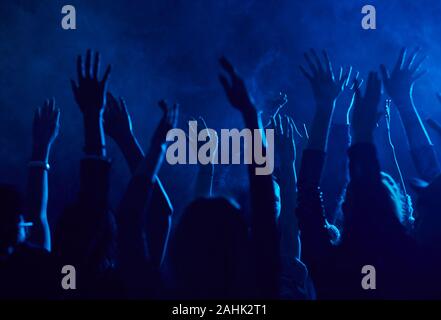 Silhouette de grand groupe de gens qui élèvent les mains tout en appréciant la musique les concerts de smoky de nuit éclairé par la lumière bleue, copy space Banque D'Images