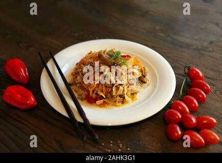 Salade de nouilles aux crevettes sur une assiette blanche et des bâtons. Salade de style coréen épicé sur une table en bois. Banque D'Images