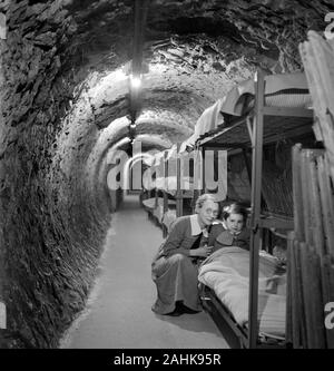 Femme agenouillée à côté du lit d'enfant en tunnel souterrain pendant la Seconde Guerre mondiale, les bombardements de Londres, Angleterre, Royaume-Uni, photo de Toni Frissell, Janvier 1945 Banque D'Images