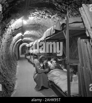 Femme agenouillée à côté du lit d'enfant en tunnel souterrain pendant la Seconde Guerre mondiale, les bombardements de Londres, Angleterre, Royaume-Uni, photo de Toni Frissell, Janvier 1945 Banque D'Images
