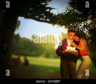 Jeune femme debout avec son bras autour d'un homme alors qu'il est titulaire d'un gâteau d'anniversaire. Banque D'Images