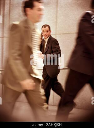Vue latérale d'un homme parle sur son téléphone cellulaire tout en marchant le long d'un couloir. Banque D'Images