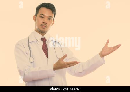 Studio shot of young Asian man médecin montrant quelque chose Banque D'Images