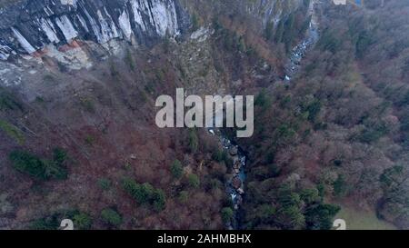 En vue de l'op d'un drone de la gorge de la rivière qui coule à travers un paysage alpin forêt brumeuse sur un hivers brumeux jour. Banque D'Images