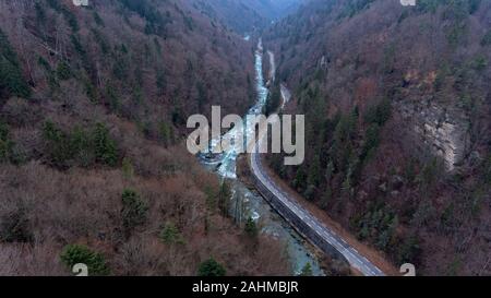 En vue de l'op d'un drone de la gorge de la rivière qui coule à travers un paysage alpin forêt brumeuse sur un hivers brumeux jour. Banque D'Images