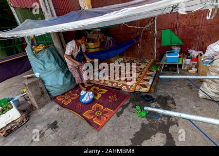 Une femme asiatique vivant dans la rue qui gagne sa vie à partir de bidons d'évacuation & carton compte son argent à son refuge à Kampong Cham, Cambodge Banque D'Images