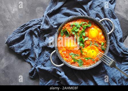 Shakshuka dans une casserole sur fond rustique gris. Plats traditionnels du Moyen-Orient. Œufs frits avec légumes. Espace pour le texte. Vue de dessus. Banque D'Images