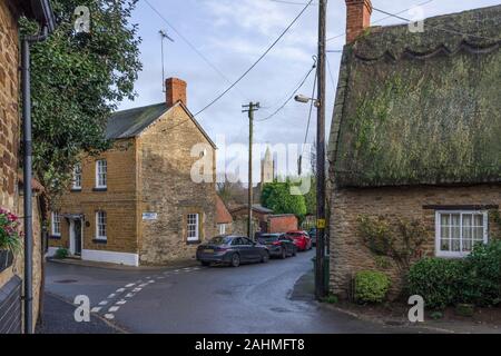 Scène de rue d'hiver dans le joli village de Milton Malsor, Northamptonshire, Royaume-Uni ; maisons, toit de chaume et un lointain clocher d'église. Banque D'Images