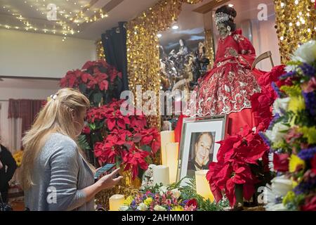 Un joli Santa Muerte prêtresse dirige un service dans un temple d'accueil à Jackson Heights, Queens, New York. Elle lit les prières de son téléphone. Banque D'Images