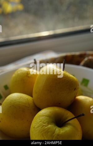 Vieux jaune naturel des pommes dans une assiette sur un rebord de fenêtre Banque D'Images