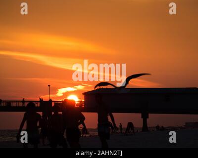 Beau coucher du soleil à Florida Beach avec des silhouettes de garçons jouant et un oiseau en vol, de la jetée en arrière-plan. Orange ciel spectaculaire avec quelques nuages. Copyspa Banque D'Images